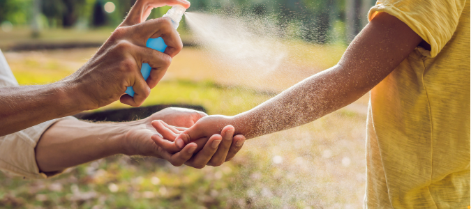 spraying skin with mosquito spray